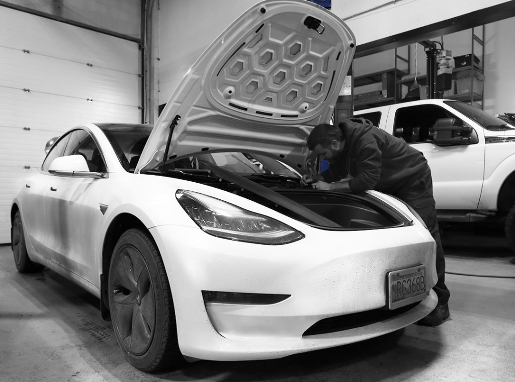 Automotive technician leaning over under the hood of Tesla performing repairs. 