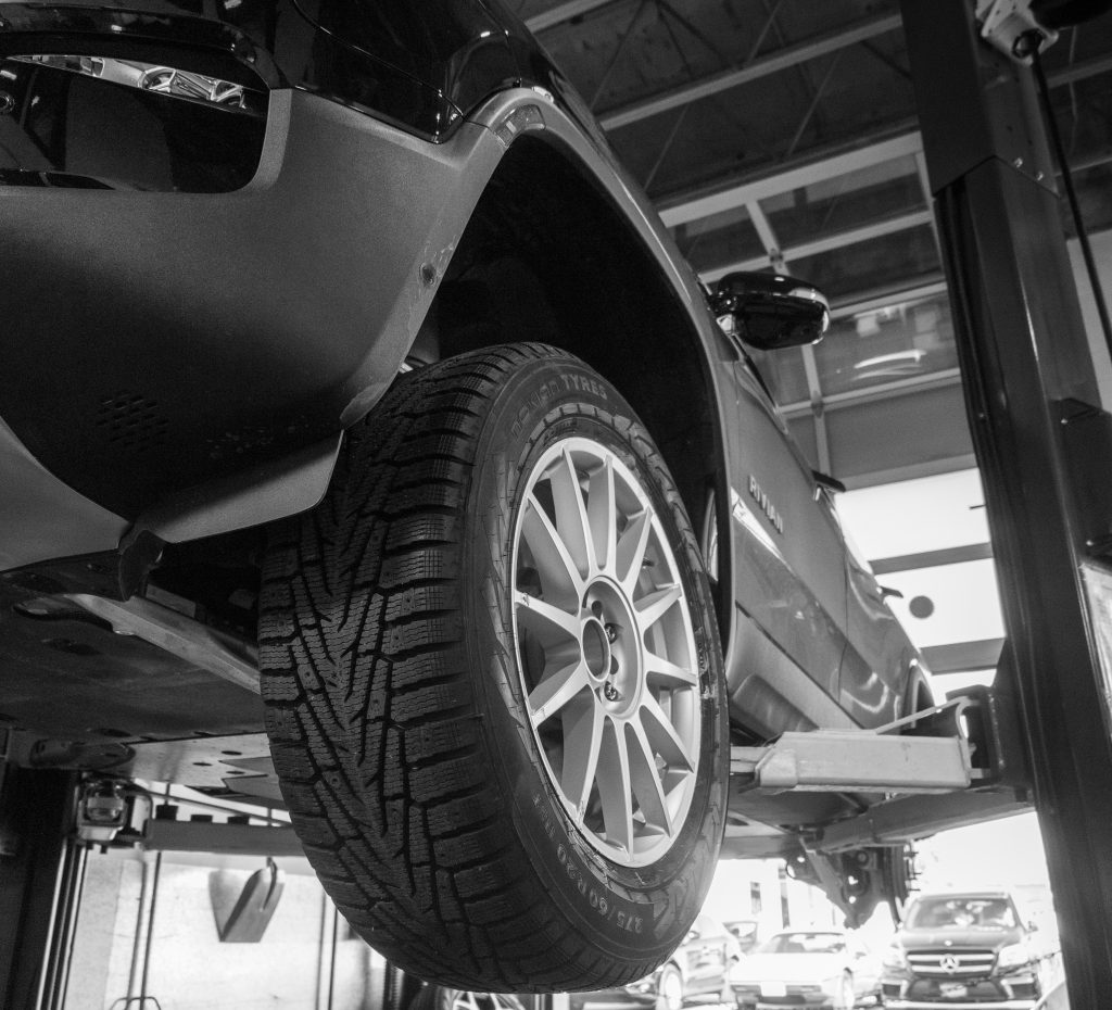 close up black and white image of a Rivian's tires while on a 4 post life in a workshop